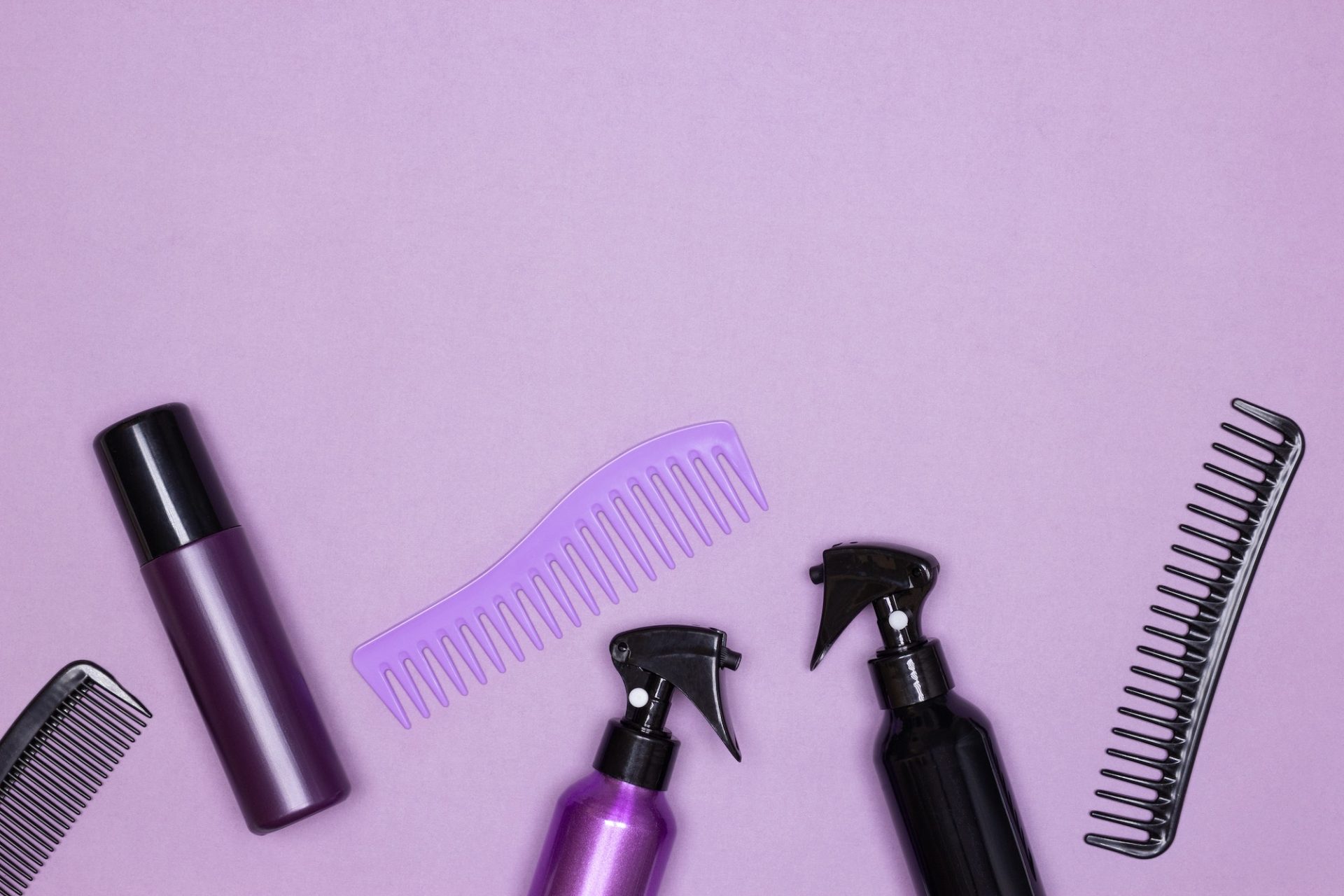Hair styling products with combs top view on purple background. Copy space