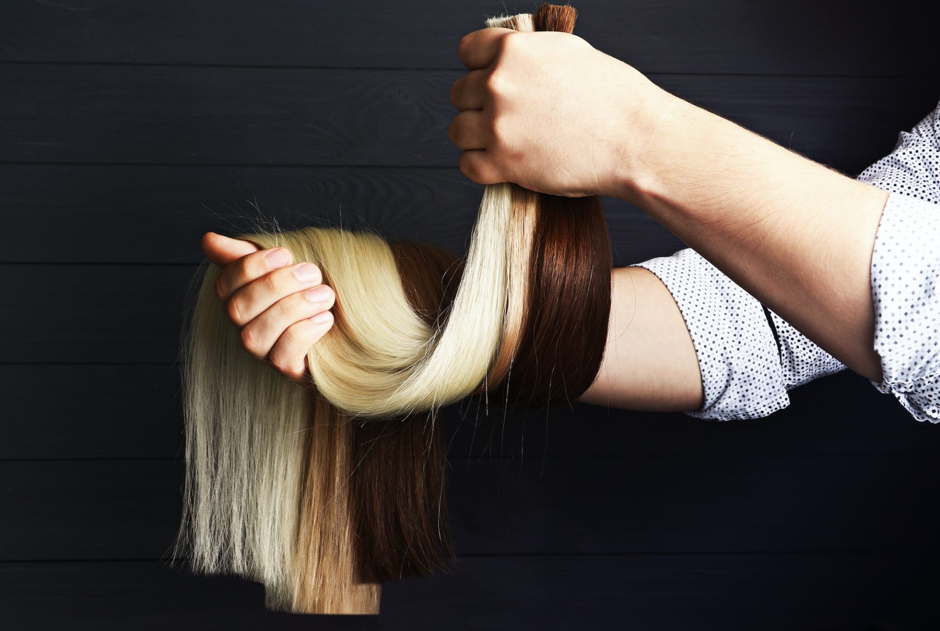 The male hand holds sections of hair for extension.